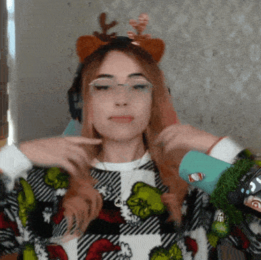 a woman wearing a grinch sweater and a reindeer headband holds her hair