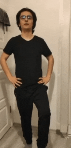 a young man wearing glasses and a black t-shirt stands with his hands on his hips