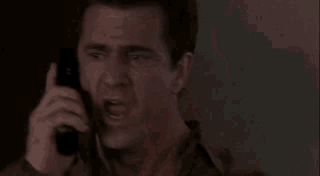 a man is talking on a cell phone with a very angry look on his face .