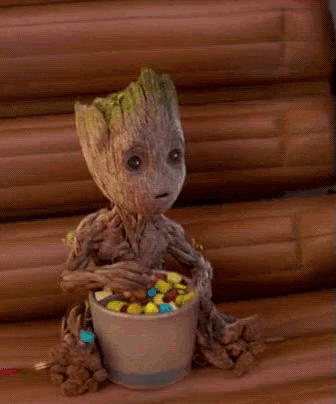 a baby groot is sitting next to a bowl of candy on a wooden table