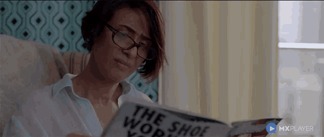 a woman wearing glasses is reading a book called the shoe world