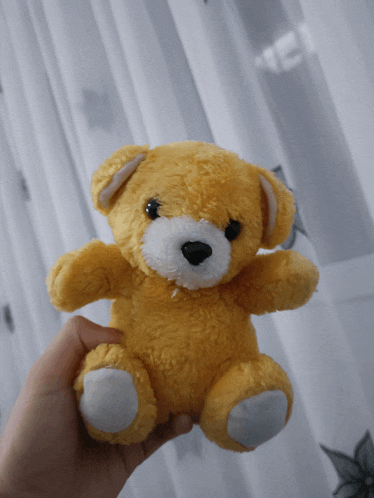 a yellow teddy bear is being held in someone 's hand