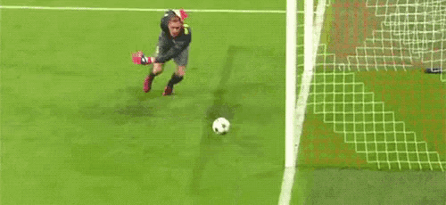 a soccer goalie is laying on the ground trying to stop a ball from going into the net .