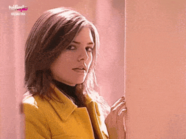 a woman in a yellow coat is standing next to a wall with the words historia fina on the bottom right