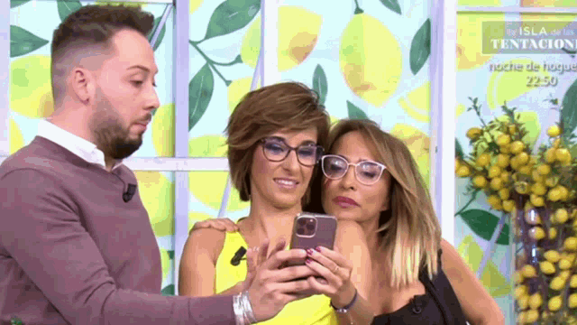 a man and two women are looking at a cell phone in front of a lemon wall
