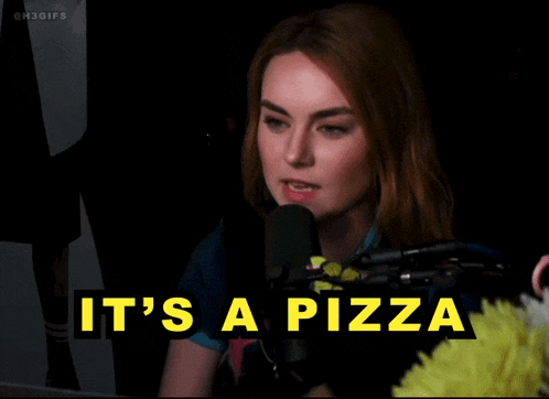 a woman speaking into a microphone with the words " it 's a pizza " behind her