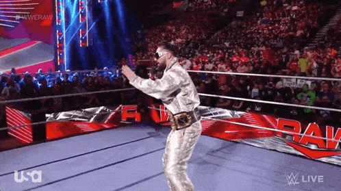 a wrestler in a silver suit is walking out of a wrestling ring .