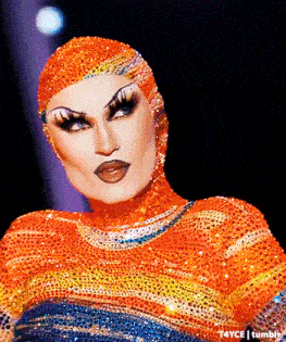 a drag queen is wearing a rainbow colored outfit with a hood on her head