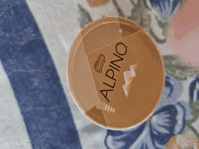 a container of nestle alpino sits on a floral cloth