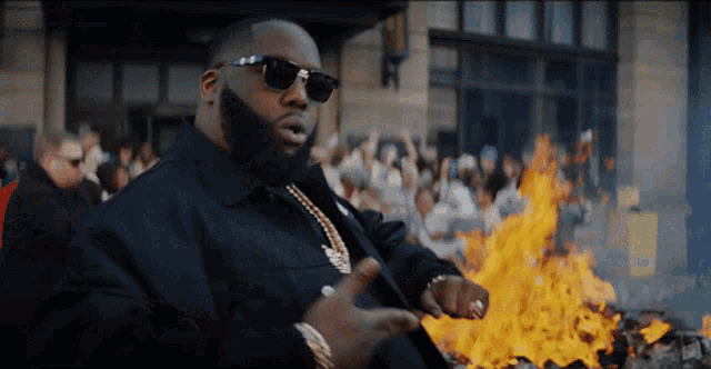 a man in sunglasses stands in front of a large fire