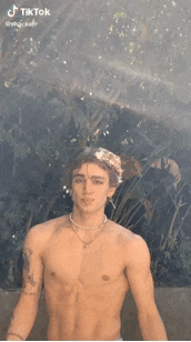 a shirtless man is standing in the rain with a necklace on his neck .