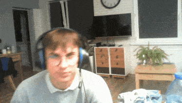a man wearing headphones in a living room with a clock on the wall behind him