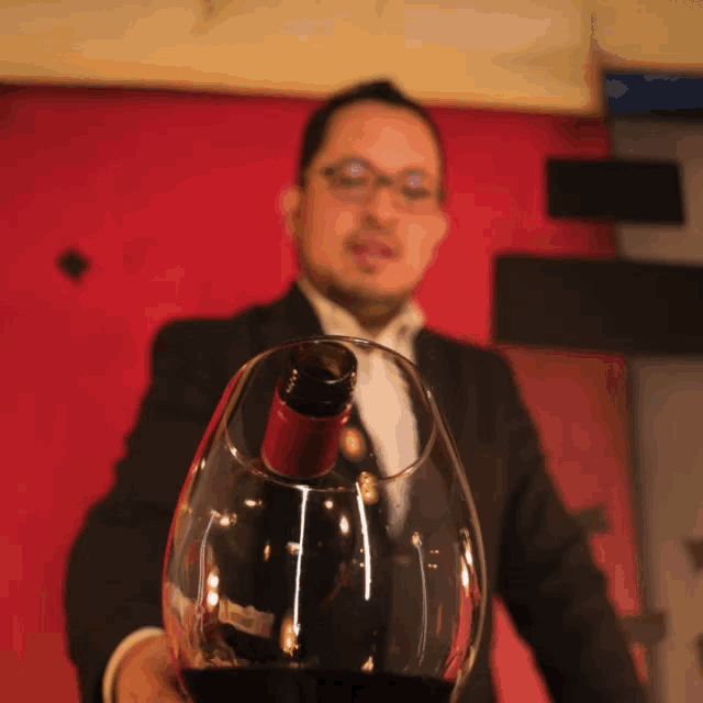 a man in a suit holds a glass of wine with a bottle of wine in it