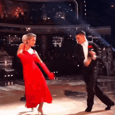 a woman in a red dress is dancing with a man in a tuxedo on a dance floor