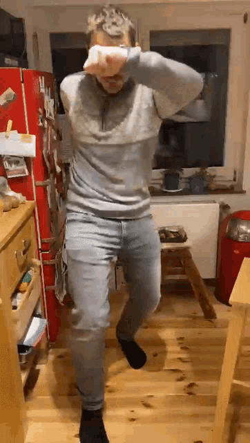 a man is dancing in a kitchen with a red refrigerator in the background