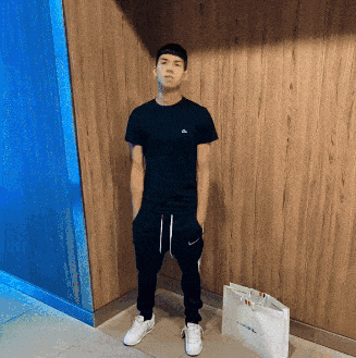 a man wearing a black shirt and nike pants stands next to a white bag