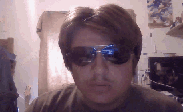 a man wearing sunglasses looks at the camera with a reflection of a computer screen