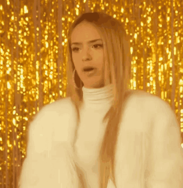 a woman is wearing a white fur coat and standing in front of a gold curtain .