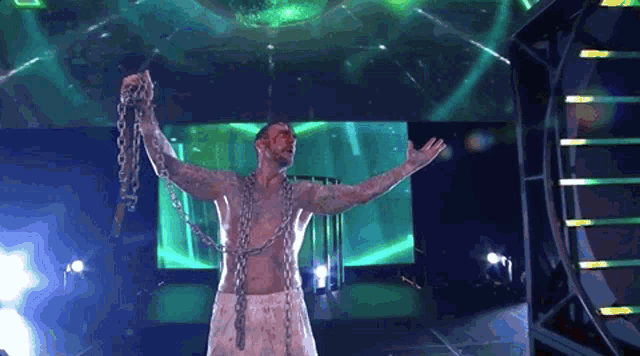 a man with chains around his neck stands in front of a large screen