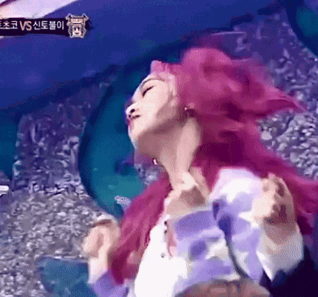 a woman with pink hair is dancing in front of a sign that says vs.