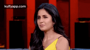 a woman in a yellow dress is sitting on a couch looking at the camera .