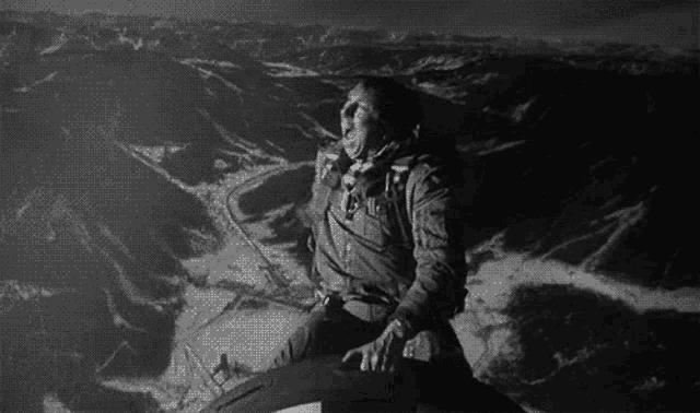 a black and white photo of a man sitting on top of a motorcycle .