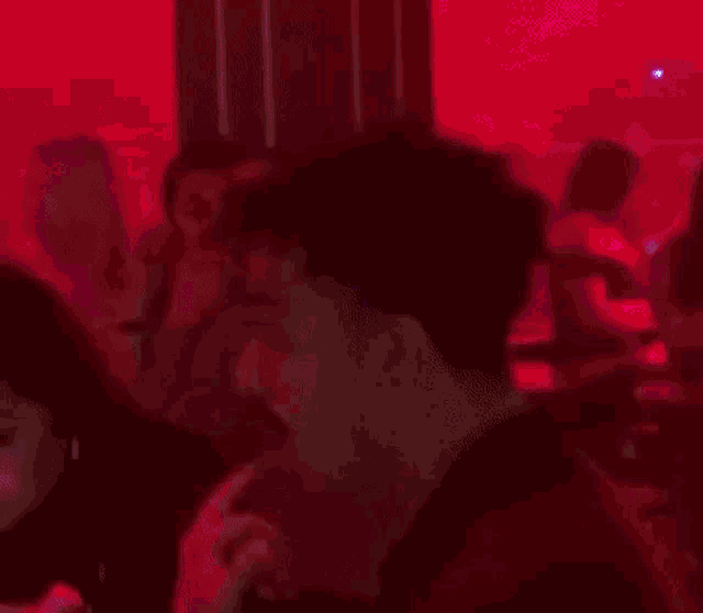 a man is singing into a microphone in a dark room with red lights behind him .