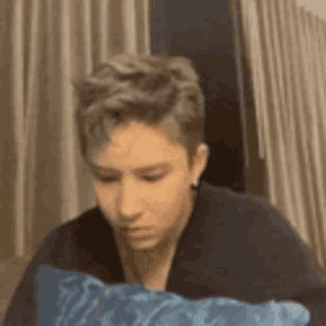 a young man is sitting in a chair with a blue pillow in his lap .