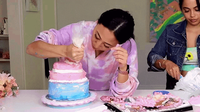 two women are decorating a pink and blue cake