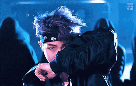 a man with blue hair and a bandana on his head is dancing in front of a microphone .