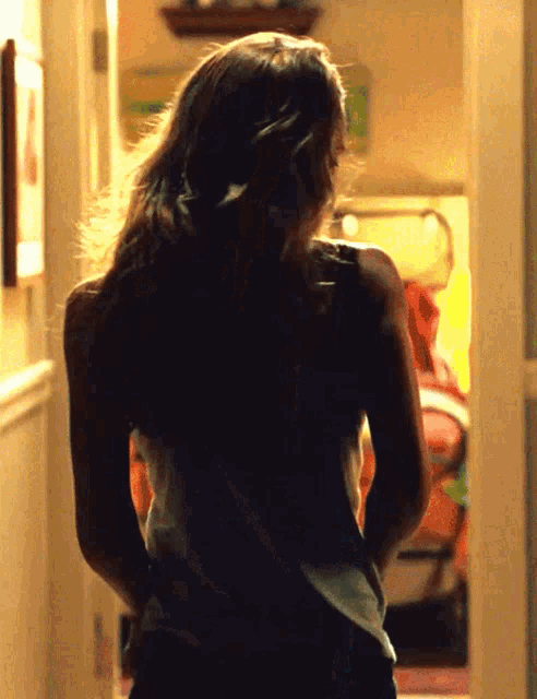 a woman in a white tank top is standing in a dark hallway