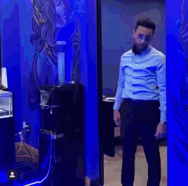a man in a blue shirt and black pants is standing in a room with a water dispenser .