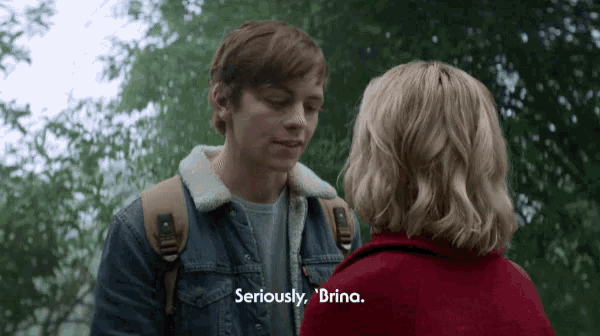 a man in a denim jacket talks to a woman in a red coat