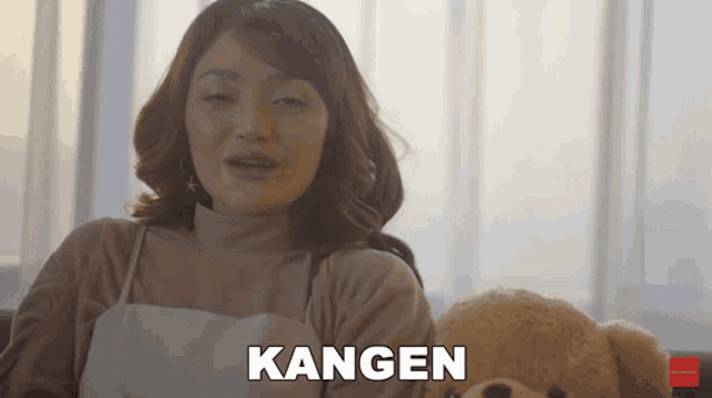a woman is sitting next to a teddy bear and the word kangen is above her head
