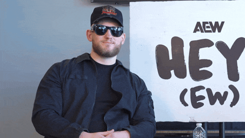 a man wearing sunglasses stands in front of a sign that says hey