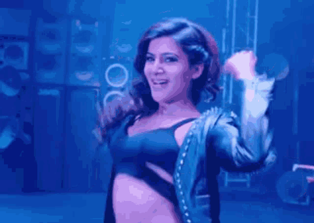 a woman in a black bra and blue jacket is dancing on a stage .