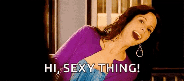 a woman in a purple sweater and blue dress is smiling and says hi sexy thing .
