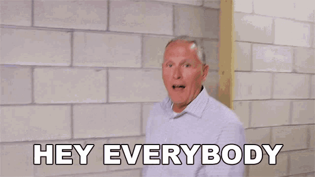 a man is standing in front of a brick wall with his arms outstretched and says hey everybody