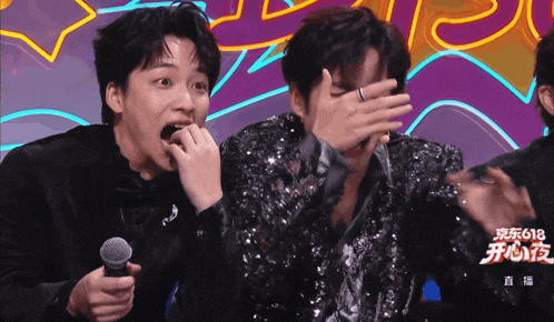 a man with a ring on his finger is covering his face while another man holds a microphone