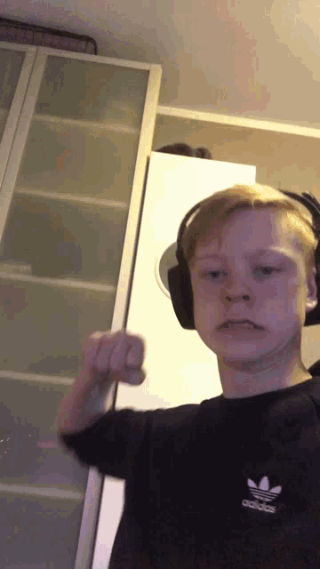 a boy wearing headphones and a black adidas shirt flexes his muscles