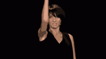 a woman in a black dress is dancing on a stage in front of a black background .