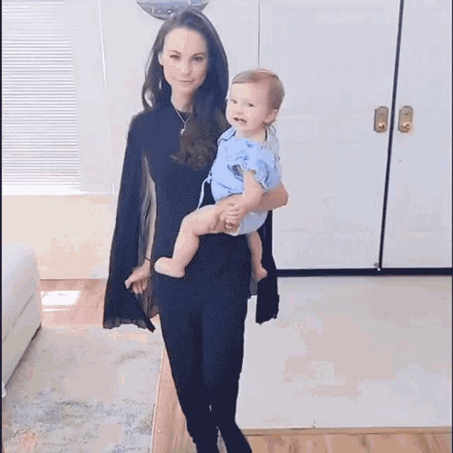 a woman is holding a baby in her arms while standing in a living room .