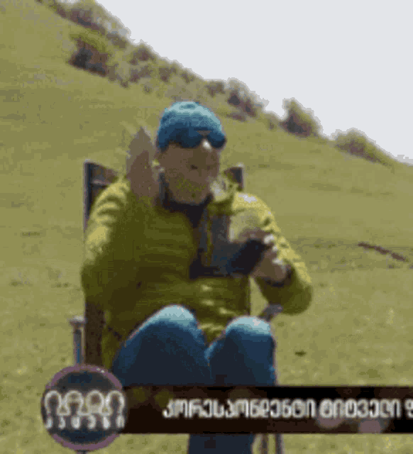 a man in a green jacket and blue hat is sitting in a chair in the grass