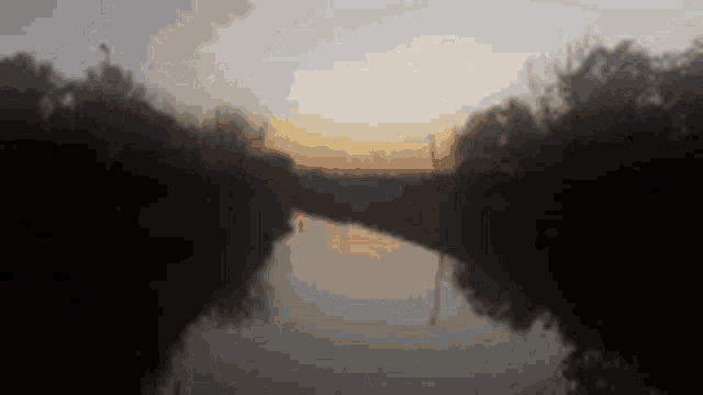 a river with a sunset in the background and trees in the foreground