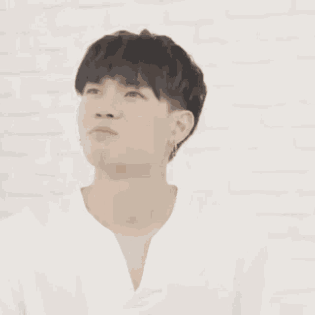 a young man in a white shirt is touching his hair with his hand .