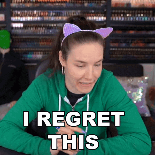 a woman in a green hoodie says i regret this while wearing cat ears