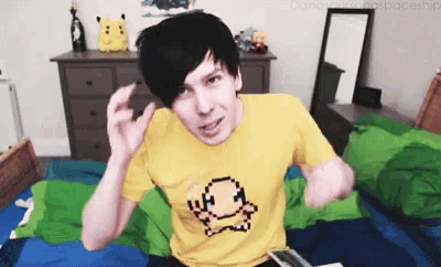 a man wearing a yellow shirt with a pokemon on it is sitting on a bed .