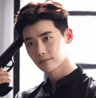 a young man is holding a gun to his head and looking at the camera .
