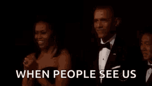 a man in a tuxedo and a woman in a strapless dress are sitting next to each other in a dark room .
