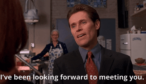 a man in a suit and tie is talking to a woman and says i 've been looking forward to meeting you